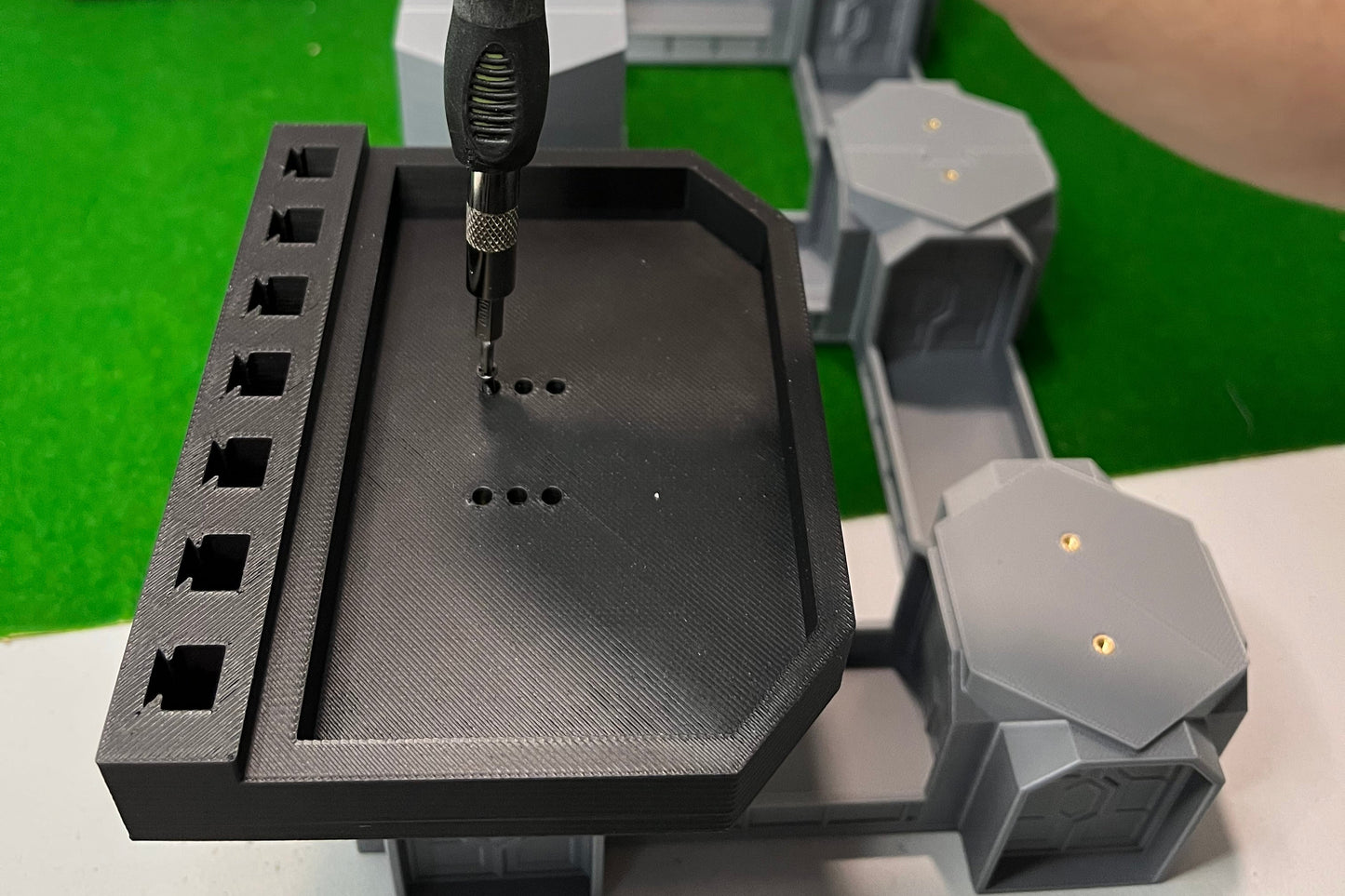 Hand using a tool to interact with a mechanical device on a green surface